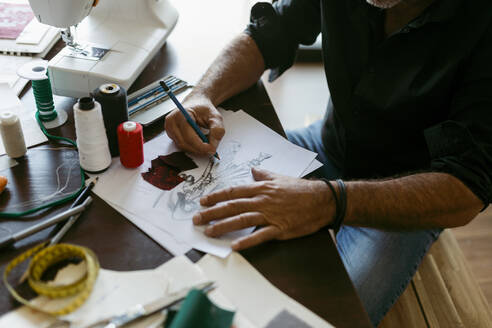 Kostümbildnerin macht Skizze auf Papier am Tisch im Arbeitsatelier - VABF03687