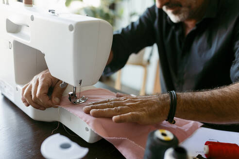 Männlicher Kostümbildner beim Nähen von Stoffen in einem Atelier - VABF03698