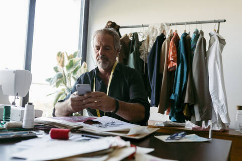 Male costume designer using smart phone while working at table in studio stock photo