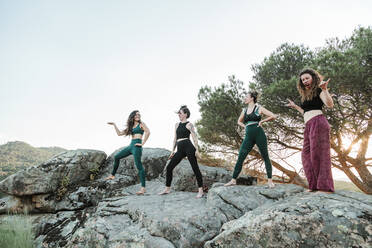 Female friends practicing yoga on rocks against clear sky during weekend - MRRF00636