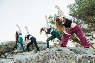 Female friends practicing yoga on rocks against clear sky during weekend - MRRF00639