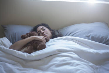 Junge Frau hält Spielzeug beim Schlafen auf dem Bett zu Hause - AJOF00434