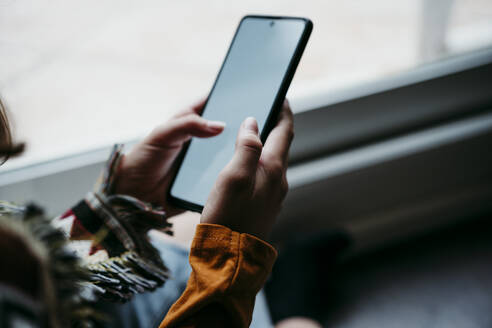 Mädchen benutzt Mobiltelefon, während sie zu Hause am Fenster sitzt - EBBF01100