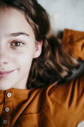 Smiling girl with hands behind head lying on floor at home - EBBF01104