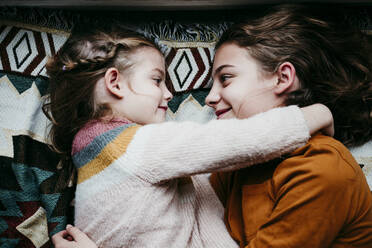 Smiling sisters with arm around lying on blanket at home - EBBF01118