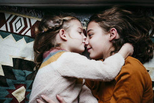 Girl kissing sister while lying on blanket at home - EBBF01119