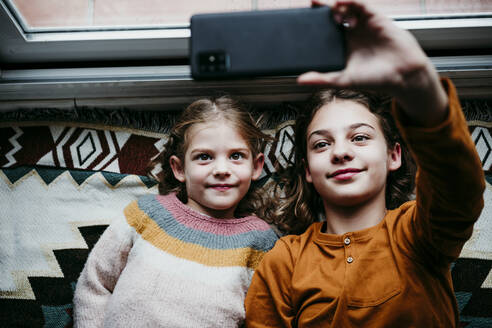 Sisters taking selfie through mobile phone while lying on blanket at home - EBBF01121