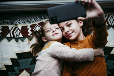 Mädchen, das seine Schwester umarmt, während es ein Selfie mit dem Handy zu Hause macht - EBBF01122