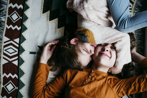 Girl embracing sister face while lying on blanket at home - EBBF01126