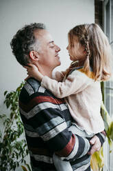 Father looking at daughter while carrying in arms at home - EBBF01142