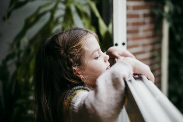 Mädchen schaut durch das Fenster, während sie zu Hause steht - EBBF01149