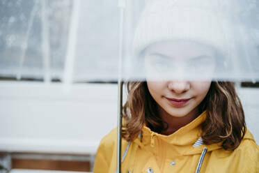 Girl wearing raincoat hiding face under umbrella outdoors - EBBF01153