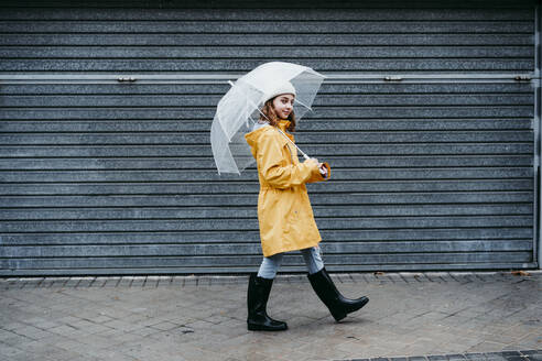 Girl wearing raincoat and jump boot walking on sidewalk outdoors - EBBF01155