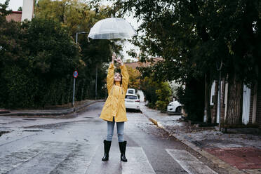Girl wearing raincoat and jump boot standing on road in city - EBBF01161