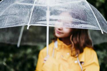 Mädchen im Regenmantel, das einen Regenschirm hält, während es im Freien steht - EBBF01164