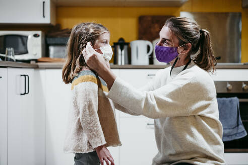 Mother adjusting daughter face mask while sitting at home - EBBF01182