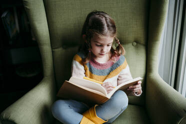 Nettes Mädchen schreibt in einem Buch, während sie auf einem Stuhl zu Hause sitzt - EBBF01186