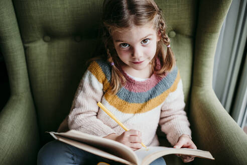 Cute girl doing homework while sitting on chair at home - EBBF01190