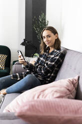 Young woman using mobile phone while sitting on sofa at home - GIOF09329