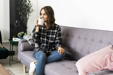 Woman drinking coffee while sitting on sofa at home - GIOF09330