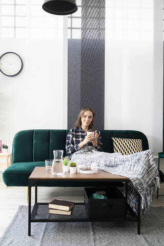 Young woman drinking coffee while relaxing on sofa at home stock photo