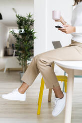 Businesswoman with coffee cup using mobile phone while sitting on table at office - GIOF09378