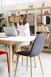 Geschäftsfrau, die ein Mobiltelefon benutzt, während sie im Büro sitzt - GIOF09388