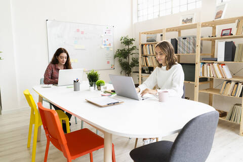 Young women working on laptop while sitting by table at office stock photo
