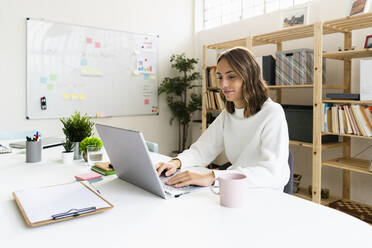 Businesswoman working on laptop while sitting by table at office - GIOF09392