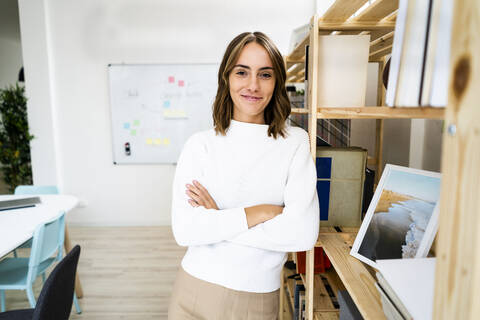 Smiling confident businesswoman standing with arms crossed at office stock photo