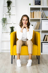 Lächelnde Geschäftsfrau sitzt mit dem Kopf in den Händen auf dem Sofa im Büro - GIOF09396