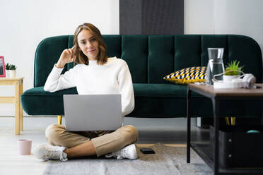 Smiling businesswoman using laptop while sitting on floor at office - GIOF09404