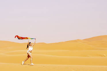 Frau läuft mit Regenbogenflagge auf Sand beim Dessert - GGGF00015