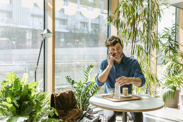 Lächelnder Geschäftsmann, der mit seinem Handy telefoniert, während er am Tisch im Café sitzt - VABF03739
