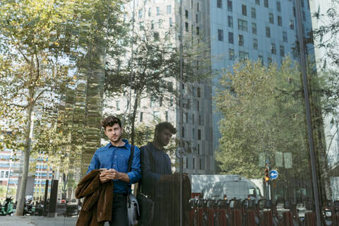 Confident handsome young businessman leaning on glass wall of modern office building stock photo