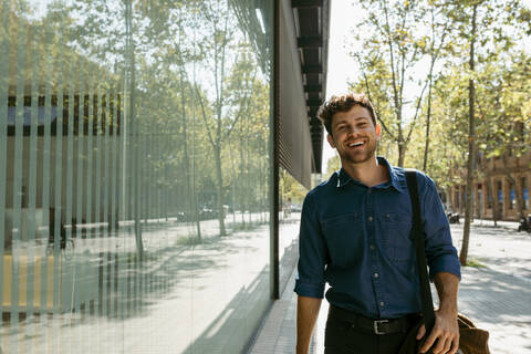 Happy young businessman walking on footpath in city during sunny day stock photo