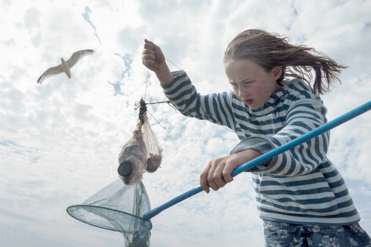 Girl catching crab in fishing net against cloudy sky stock photo