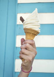 Close-up of girl's hand holding ice cream cone against striped wall - AJOF00444