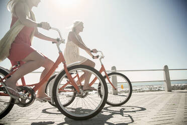 Junge Freundinnen radeln an einem sonnigen Tag auf der Promenade am Strand - AJOF00456