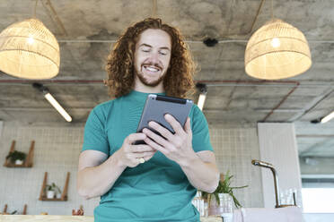 Handsome man holding digital tablet and smiling at home - FMKF06641