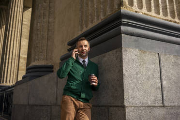 Geschäftsmann, der mit seinem Handy telefoniert und sich an eine Säule der Kasaner Kathedrale in Sankt Petersburg, Russland, lehnt - VPIF03181