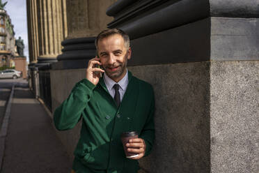 Smiling businessman talking on mobile phone while leaning on pillar of Kazan Cathedral at Saint Petersburg, Russia - VPIF03182