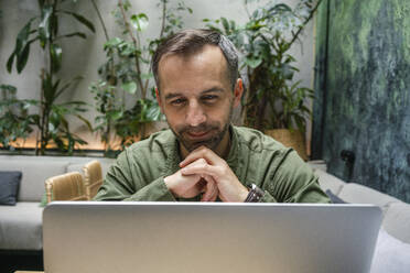 Businessman with head in hands working on laptop while sitting at cafe - VPIF03191