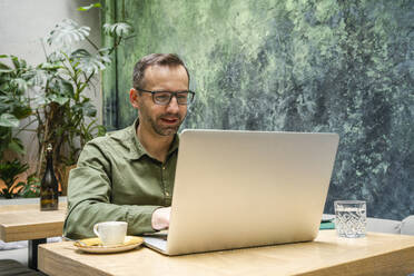 Smiling businessman working on laptop while sitting at cafe - VPIF03194