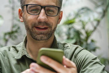 Lächelnder Geschäftsmann, der in einem Café ein Mobiltelefon benutzt - VPIF03202