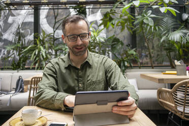 Lächelnder Geschäftsmann, der ein digitales Tablet benutzt, während er in einem Cafe sitzt - VPIF03213