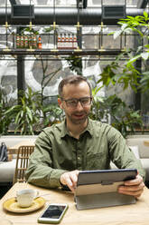 Geschäftsmann, der in einem Café sitzt und an einem digitalen Tablet arbeitet - VPIF03214