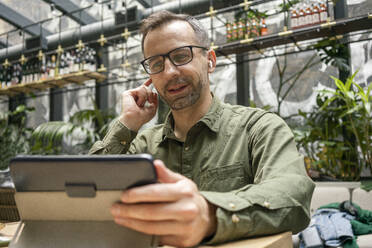 Businessman adjusting in-ear headphones while using digital tablet at cafe - VPIF03215