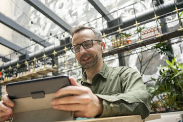 Lächelnder Geschäftsmann mit In-Ear-Kopfhörern, der ein digitales Tablet benutzt, während er in einem Café sitzt - VPIF03216