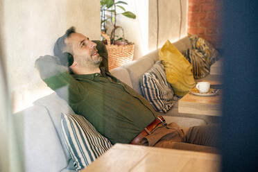 Businessman wearing headphones relaxing with hands behind head while sitting on sofa at cafe - VPIF03225